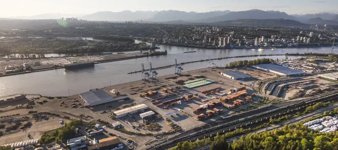 A river runs horizontally through the image. A city and mountains can been seen on the top bank and a port terminal is on the bottom bank.