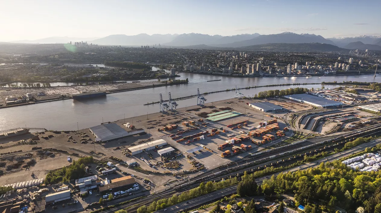 A river runs horizontally through the image. A city and mountains can been seen on the top bank and a port terminal is on the bottom bank.