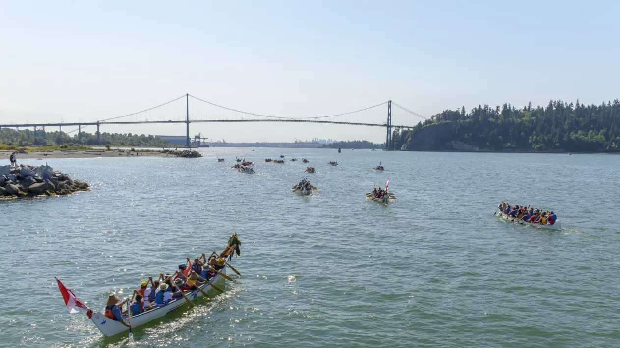 Paddlers in canoes on the water. The Lions Gate Bridge can be seen in the background.