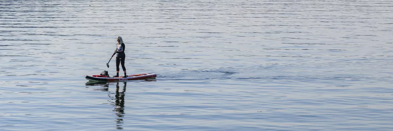 Someone steers a stand-up paddleboard on the water.