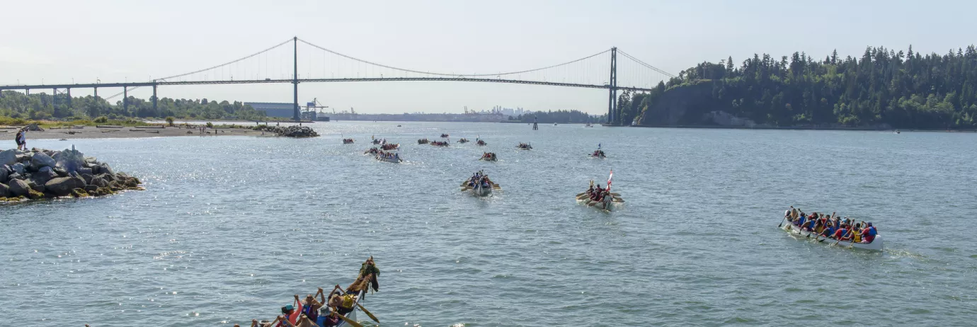 Paddlers in canoes on the water. The Lions Gate Bridge can be seen in the background.